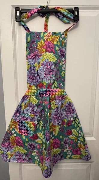 A teal floral apron with a rainbow houndstooth waistband hanging on a door.