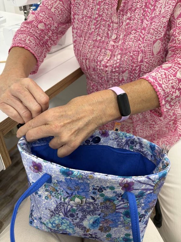 Hands clipping the lining into a finished blue floral handbag.