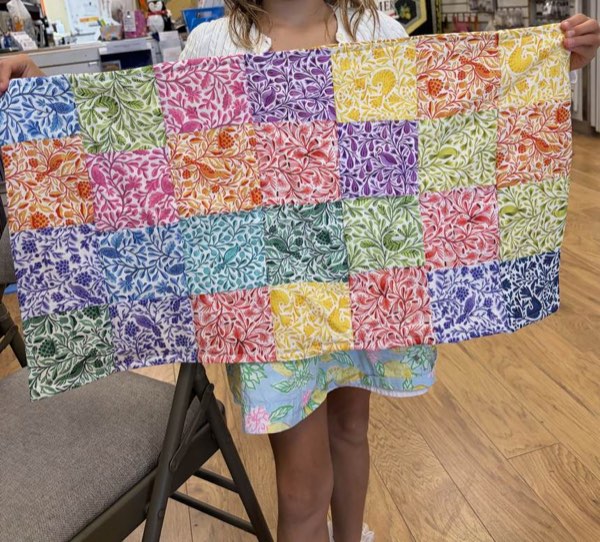 A student holding up a colourful patchwork quilt top.