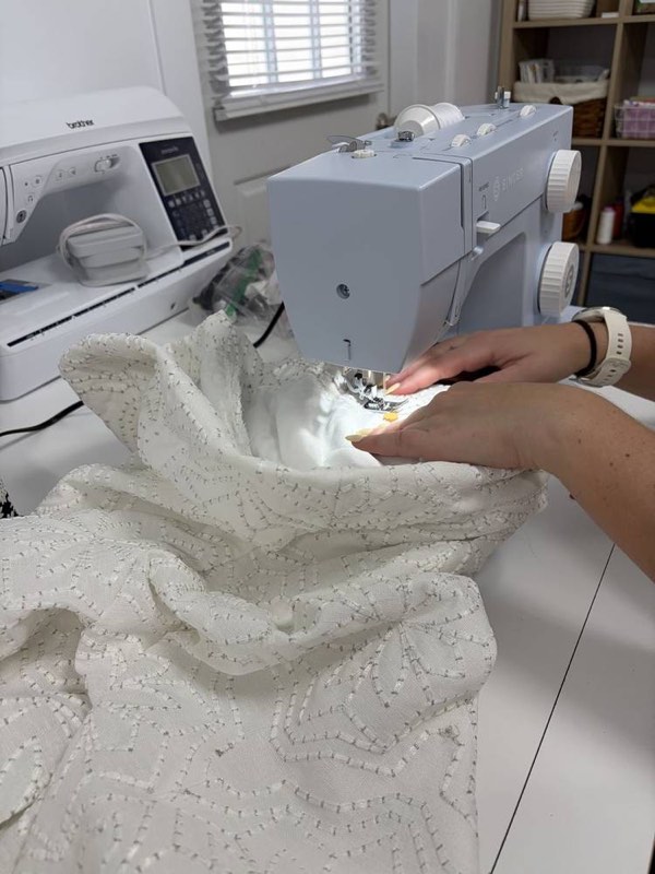 A student guiding white embroidered fabric through a sewing machine.