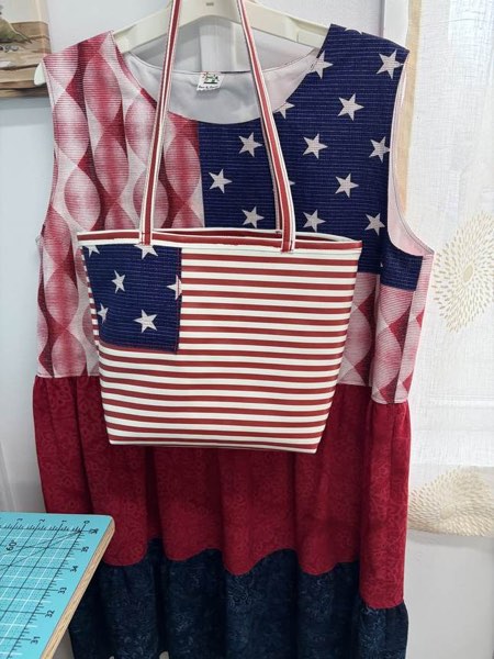 A red, white and blue tote bag hanging in front of a matching flag-print dress.