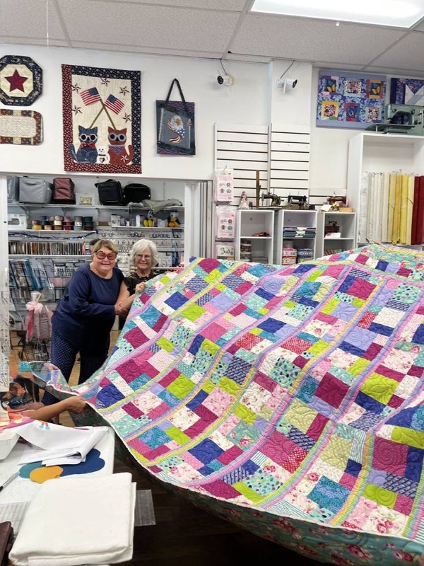 Two students holding up a large finished patchwork quilt.