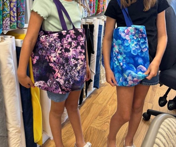 Two young students holding the floral tote bags they sewed.