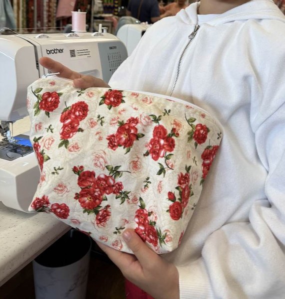 A student holding a finished zippered pouch in a red rose print.